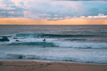 Fototapeta premium Silhoette of surfer at sunrise over Maroubra beach in Sydney Australia