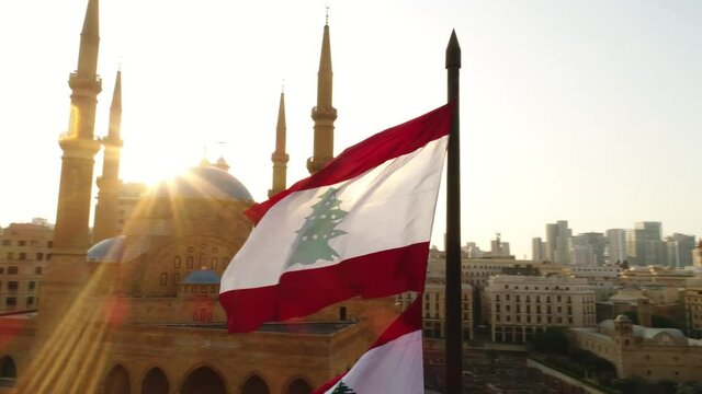 Beirut, Lebanon 2019: sunset turn around right drone shot on Lebanese flag with mosque, church and sun flaring in the background during the Lebanese revolution