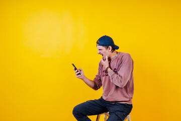 a white man in a cap with a phone in his hands is filmed on a yellow background, a hipster shows emotions