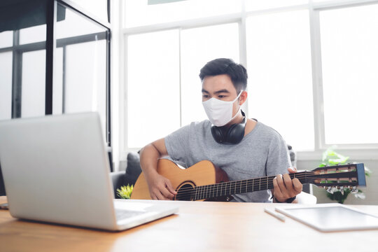 Work from home playing guitar writing composing songs free time spending activity using laptop wearing face mask self isolation quarantine lockdown staying safe in protection from coronavirus covid-19