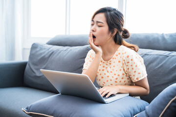 Asian businesswoman work at home using computer laptop technology freelance business plan strategy tired sleepy yawning working from home living room modern office during coronavirus COVID-19 pandemic
