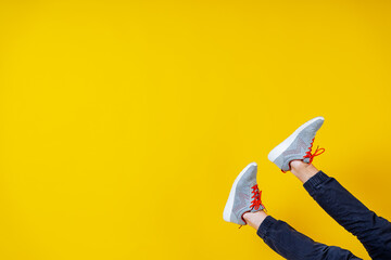feet sticking out from the bottom in sneakers on a yellow background, red laces, a concept for a fashion blog or magazine, a minimalistic Shoe background, sports