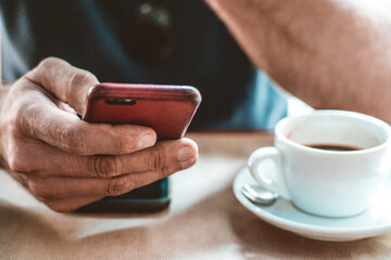Man in cafe, having a coffee while looking at his mobile phone/ cell phone