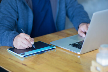 Man working on laptop and male writing on Wacom on table.