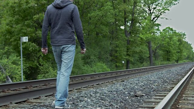 High quality 4k video of a young man who is walking on the railway away from the camera, focus on legs. Men wearing jeans and sport jacket.