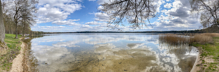 Obraz premium spring landscape on a lake with cloudy blue sky reflection in the water surface. wide panoramic view. Svityaz lake, Belarus. 