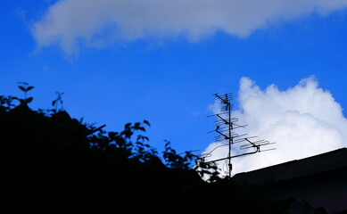 Closeup silhouette image of obsolete outdoor antenna installed on rooftop of a building against blue sky and white cloud 