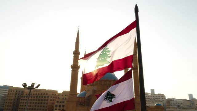 Beirut, Lebanon 2019: sunset low angle turn around drone shot with Lebanese flag in foreground, mosque, church and sun flaring in the background during the Lebanese revolution