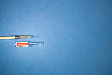 Ampola de dexametasona, em portugu&ecirc;s, com seringa em fundo azul.