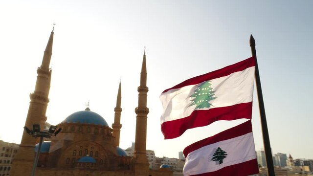 Beirut, Lebanon 2019: sunset low angle turn around slow motion drone shot with Lebanese flag in foreground, mosque, church and sun flaring in the background during the Lebanese revolution