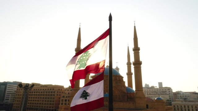 Beirut, Lebanon 2019: sunset low angle turn around left drone shot with Lebanese flag in foreground, mosque, church and sun flaring in the background during the Lebanese revolution