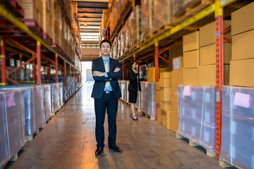 Portrait of warehouse worker with business people with crossed arms standing in a large warehouse.