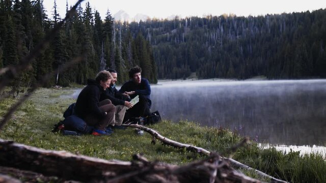Three guys camping by a lake reading a map