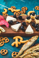 Snack board with sausage slices, cheese cubes and black olives with crackers and dry fish