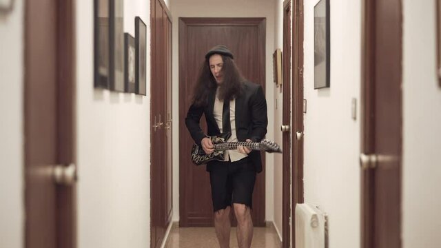 Young man in AC/DC outfit plays inflatable guitar in apartment hallway