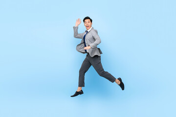Fototapeta na wymiar Full length fun portrait of happy ecstatic young Asian businessman jumping in mid-air isolated on studio blue background