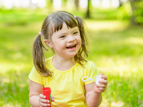 Laughing girl with syndrome down blows bubbles in a summer park
