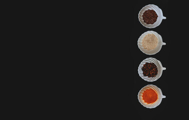 Fototapeta premium A border of spices and grains in white cups on a black isolated background. Top view