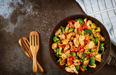 Stir-fried chicken with broccoli, bell pepper on dark background.