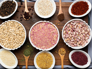 Various beans in white plates on a wooden board and spices in wooden spoons