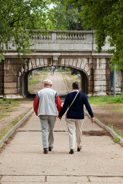 Well Dressed Lively Elderly Couple Is Showing Their Love By Holding Hands As They Stroll In A Park On A Beautiful Afternoon.