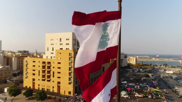 Beirut, Lebanon 2019: sunset turn around slow motion close up drone shot with Lebanese flag in foreground, mosque, church and sun flaring in the background during the Lebanese revolution