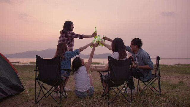 Full body shot : Young happy friends drinking beer and having fun at beach  together. Asian teenager toasting beer and enjoy together in evening on side lake. Friendship and celebration concept.