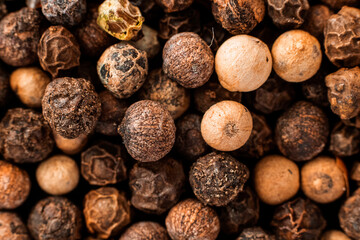 Closeup dry whole black pepper in corns. Macro background. Horizontal shot for wallpaper and postcard about culinary, herbs and spices for coocking and food. Top view. Brown tone