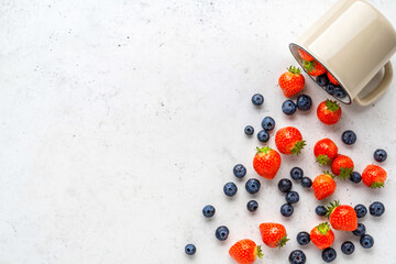 Fresh organic blueberry and strawberry in enameled mug on vintage white stone table.