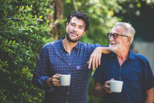 An adult hipster son and senior father at home, holding a cup of coffee in the morning