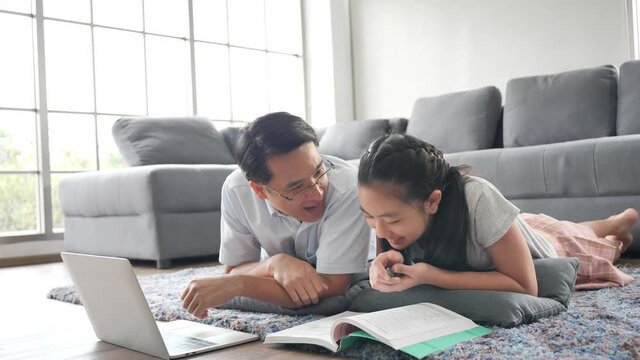 Asian Father teaches daughter books by using laptop computer Study online
