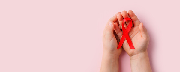Healthcare and medicine concept - kids hands holding red AIDS awareness ribbon on pink, banner for National Blood Donor Month in January, World AIDS day health living with HIV