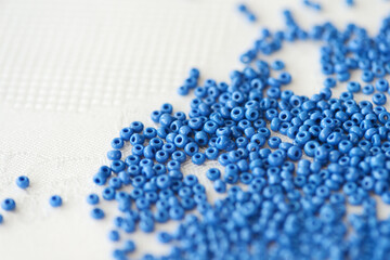 Blue seed beads scattered on a white textile background closeup. Handmade concept