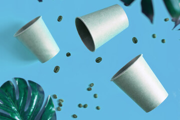 Floating eco friendly paper disposable mockup cups above blue background with green palm leaves. Zero waste
