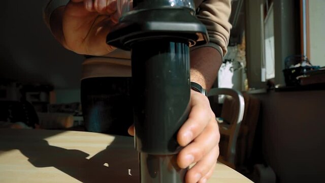 A rotating view of a transparent coffee cup being placed on top of an aeropress by a man in the background