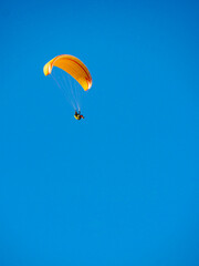 Paraglider flying in blue sky.