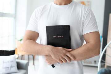 Young man with Bible at home, closeup