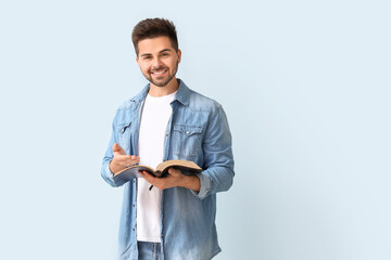 Young man with Bible on color background