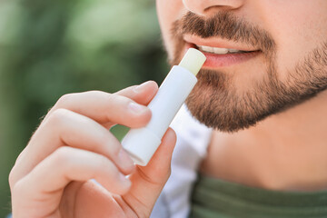 Handsome young man with lip balm outdoors, closeup - obrazy, fototapety, plakaty