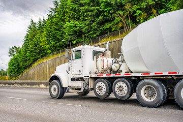 White big rig semi truck with concrete mixer trailer driving on the multiline road to construction...