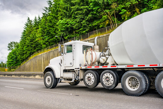 White big rig semi truck with concrete mixer trailer driving on the multiline road to construction point.
