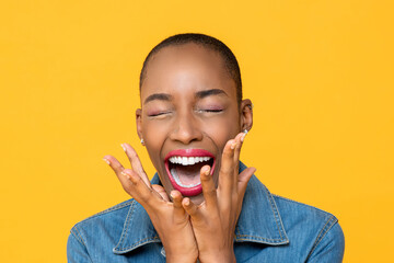 Close up portrait of ecstatic young African American woman screaming with hands covering face...