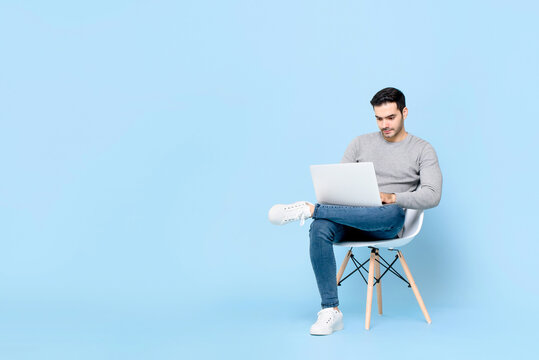 Work from home concept portrait of busy young handsome Caucasian man sitting using laptop in isolated studio blue background