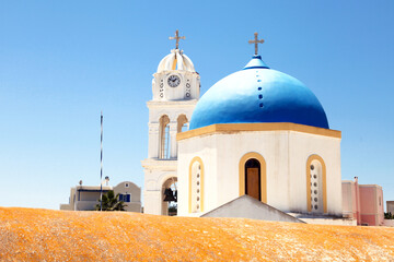A view of the blue dome and bell tower with clock of the Panagia ton Eisodion church in the traditional village of Megalochori, Santorini, Greece.