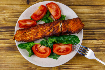 Grilled salmon fillet with spinach and tomatoes on wooden table. Top view