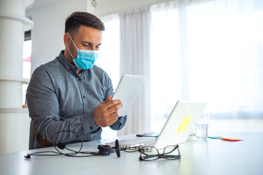 Businessman looking at a tablet PC wearing a healthcare face mask. Man in a medical mask at the office. Businessman with mask using digital tablet at work