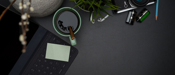 Dark modern workspace with coffee mug, wireless keyboard with notepad, supplies, decoration and copy space