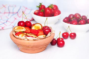 Mini tiny pancakes with straeberries and cherries on white wooden background. Trendy food concept.