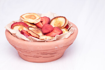 Mini tiny pancakes with straeberries and cherries on white wooden background. Trendy food concept.