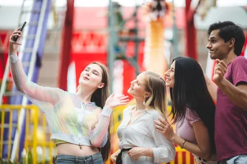 Fotobehang Friends group relaxing and taking selfie with smartphone at an amusement theme park, concept of happy and hangout carnival © chokniti